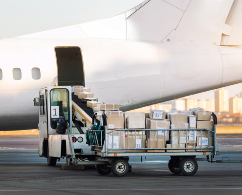 Close-up detail view of cargo cart trolley full with commercial parcels against turboprop cargo plane.