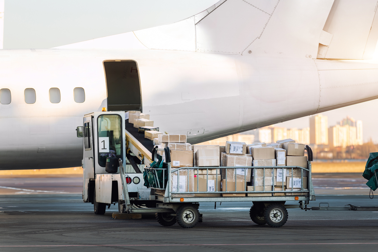 Close-up detail view of cargo cart trolley full with commercial parcels against turboprop cargo plane.